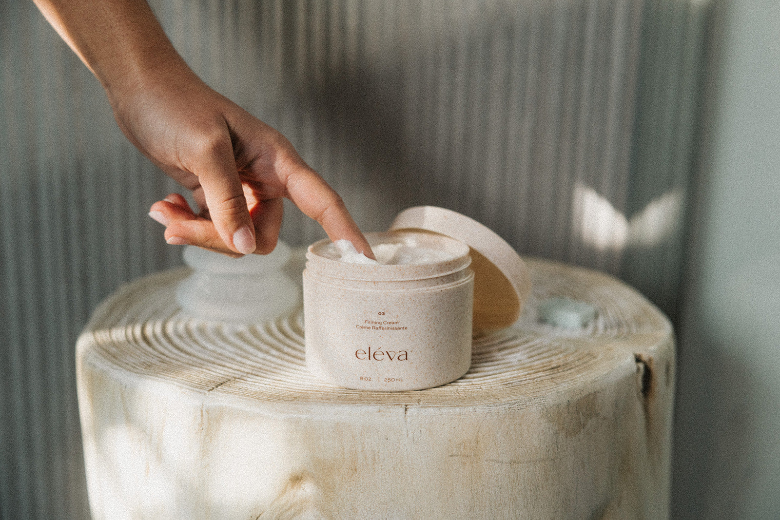 A finger dipping into Eléva firming cream on a table.